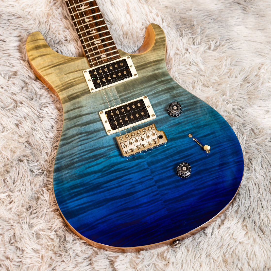 Indonesia-made PRS SE Custom 24 in Blue Fade with a flame maple top and bird inlays, resting on the bench