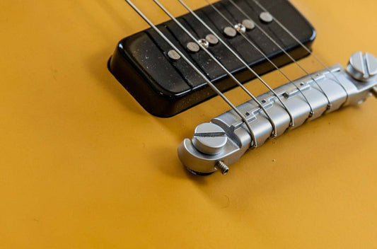 Close-up of a compensated wraparound bridge on a Gibson Les Paul Melody Maker showing the staggered ridge and stud intonation screw